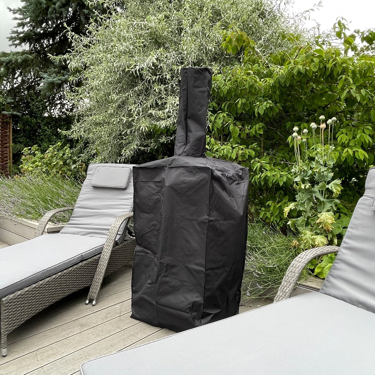 Black weather-resistant cover for the KuKoo outdoor pizza oven, protecting it from elements, set against a garden backdrop