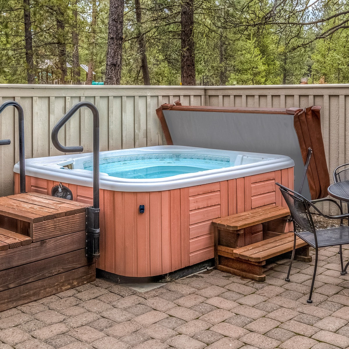 Brown 2.2m hot tub spa cover resting on a wooden deck, surrounded by trees and a stone patio, with steps leading up to it