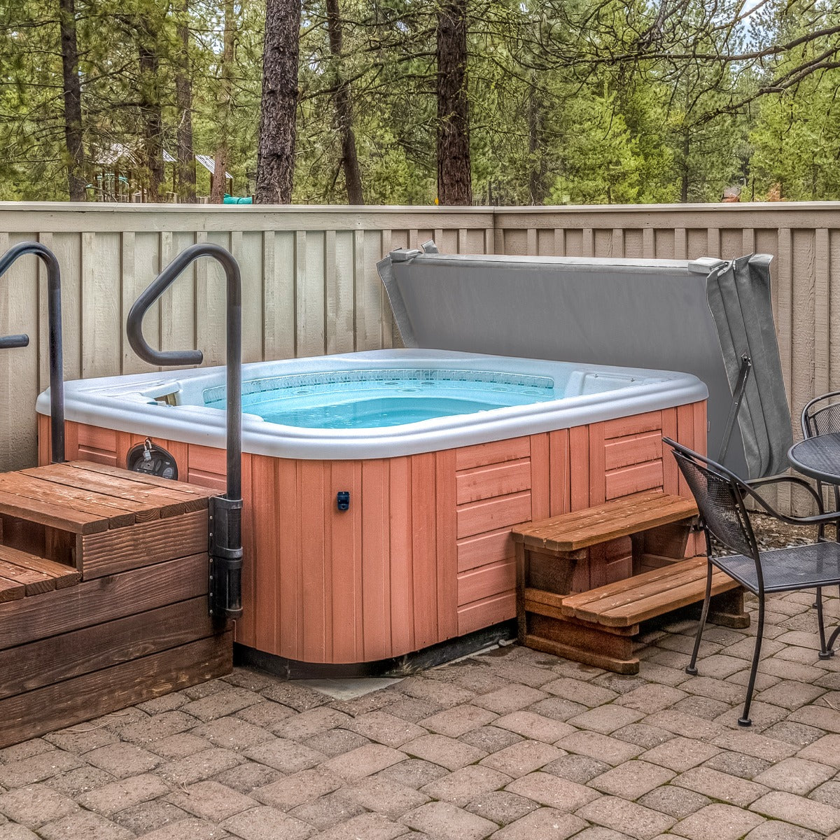 Grey hot tub spa cover resting on a 2.2m hot tub, surrounded by wooden steps and a stone patio in a serene outdoor setting