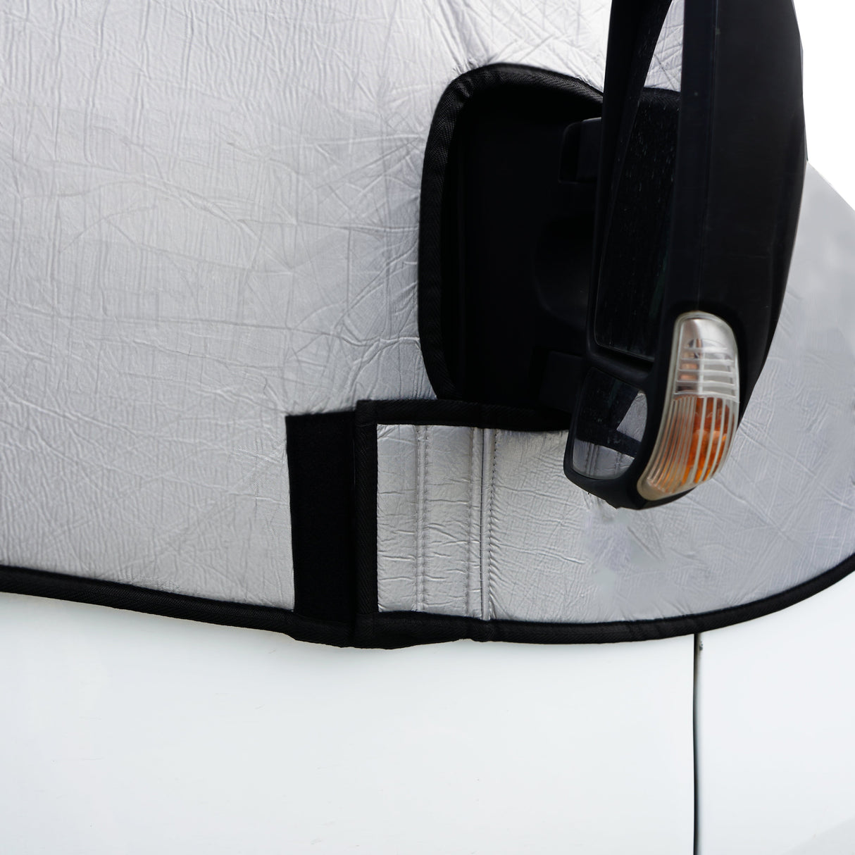 Silver motorhome screen cover with textured surface, fitted snugly around a side mirror, featuring a black Velcro strap for secure attachment