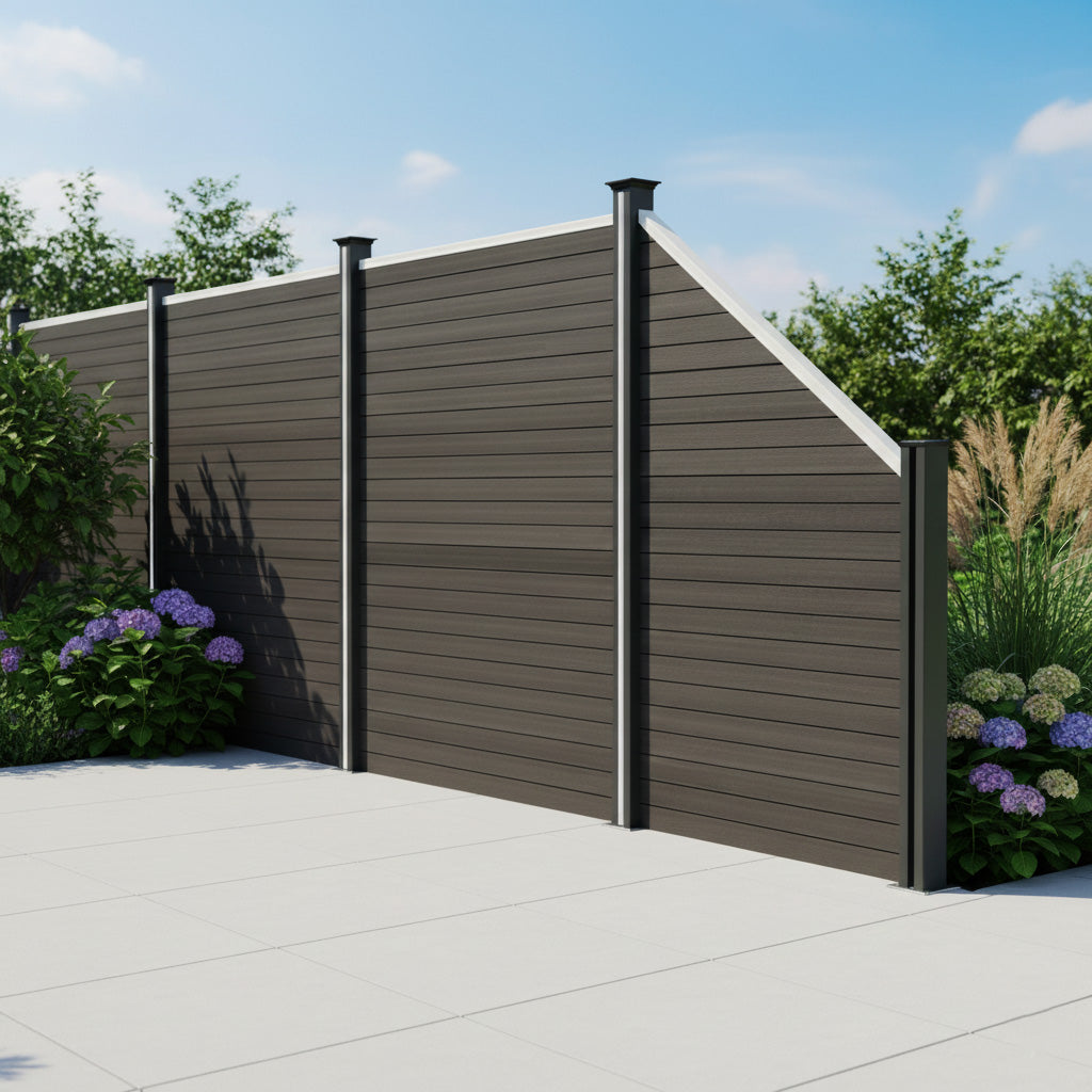 Grey composite angled fence panel with sleek horizontal slats, topped with black posts, surrounded by vibrant greenery and flowers