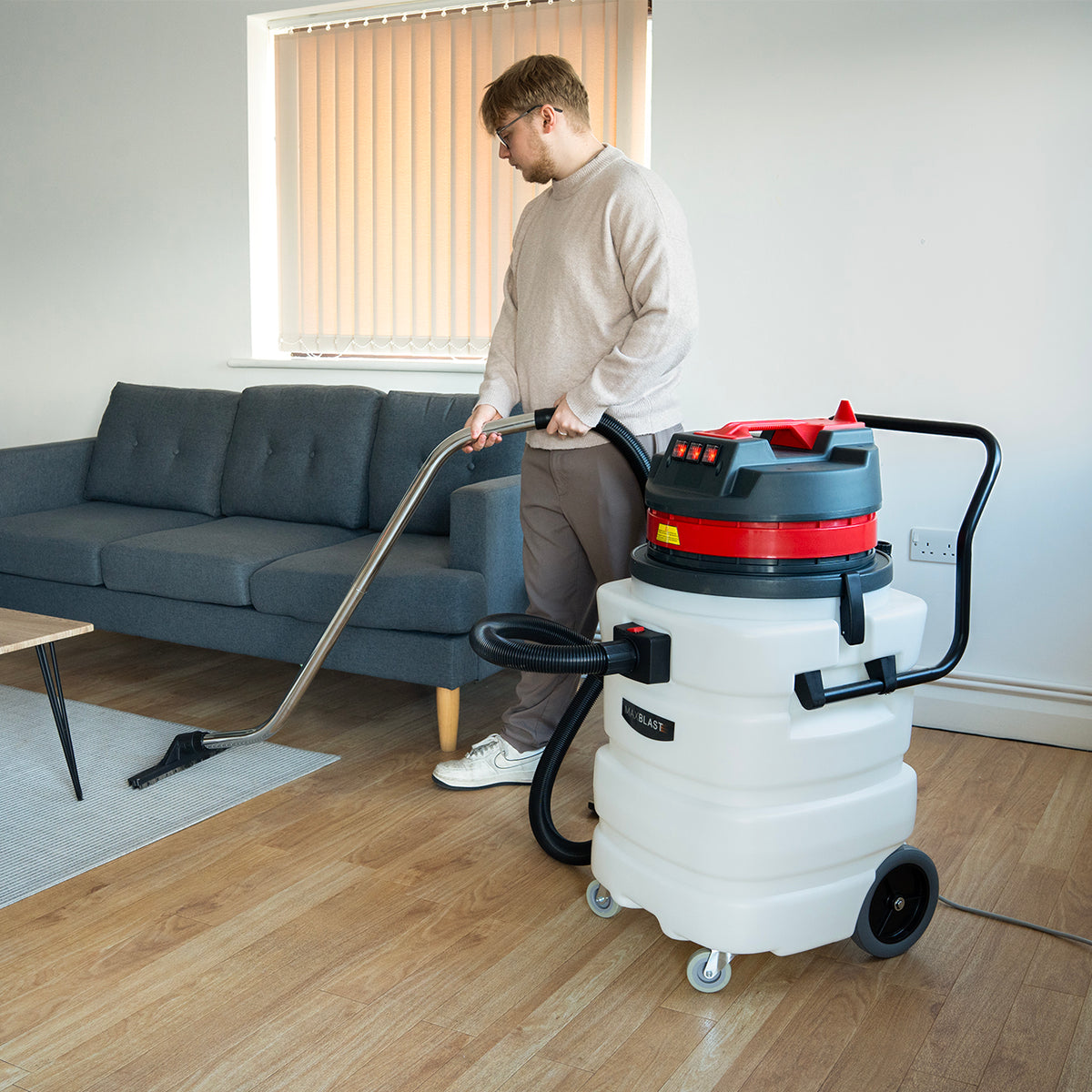 90L Maxblast industrial vacuum in white and red, being used on hardwood floor, featuring a flexible hose and metal nozzle, ideal for wet and dry cleaning