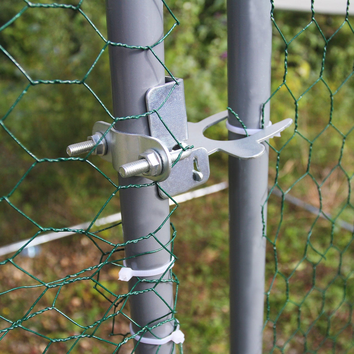 Close-up of a metal latch securing green chicken wire to a gray post, showcasing durability and easy access for poultry enclosures