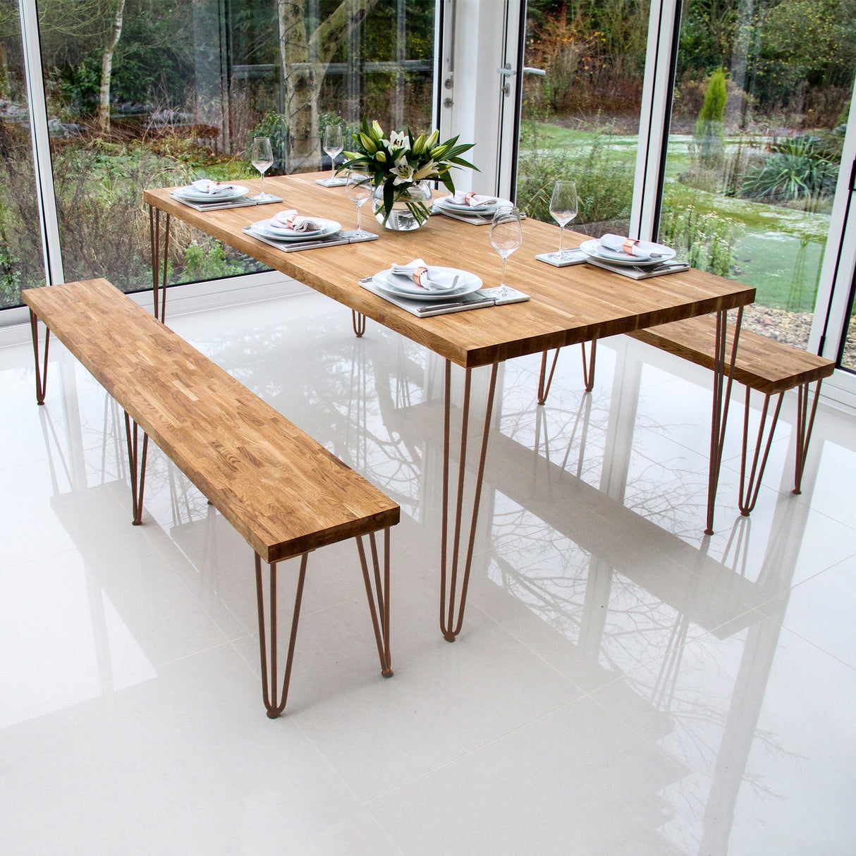 Antique copper hairpin legs support a modern wooden dining table and benches, showcasing a sleek design and warm tones