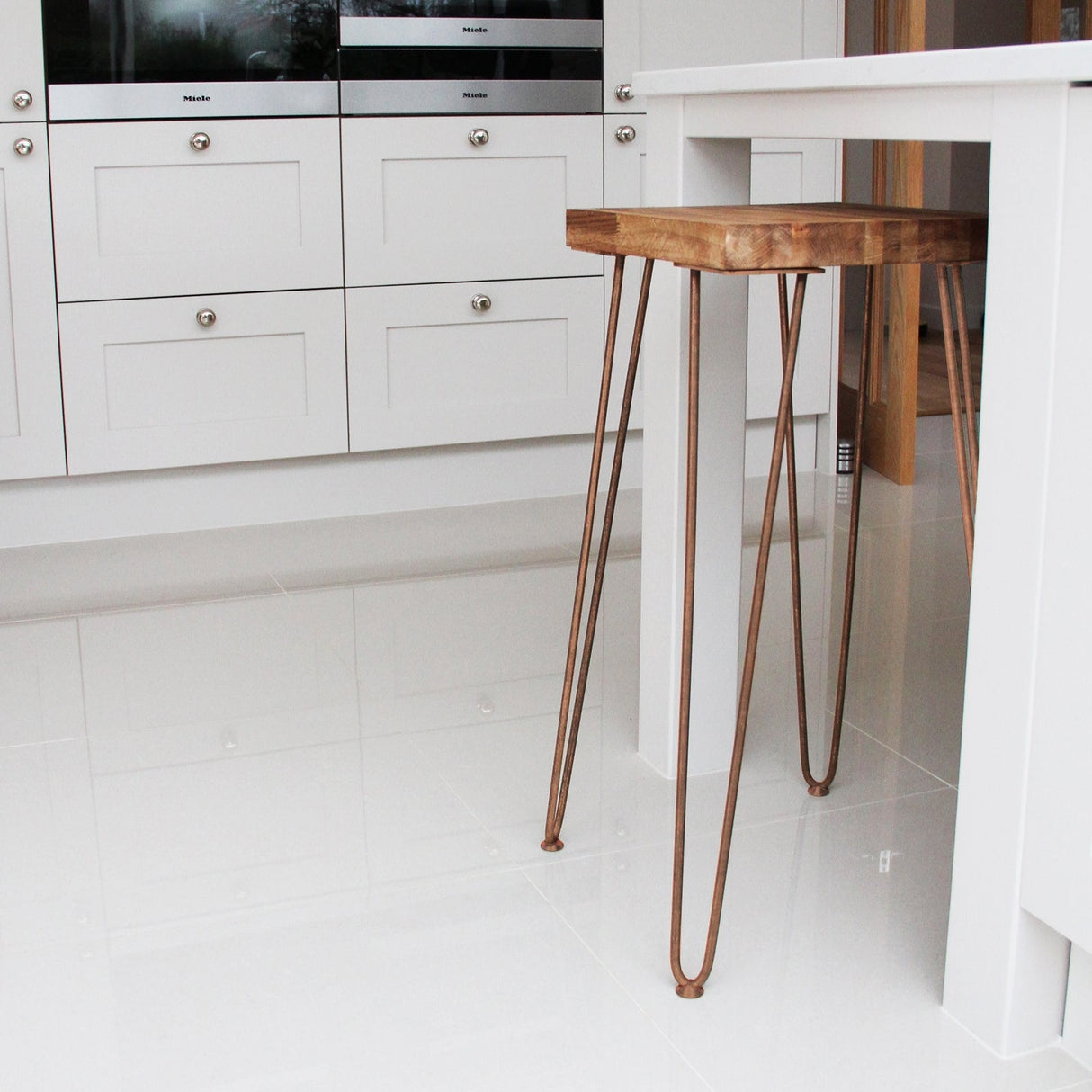 Antique copper hairpin legs with a sleek, minimalist design supporting a wooden tabletop in a modern kitchen setting