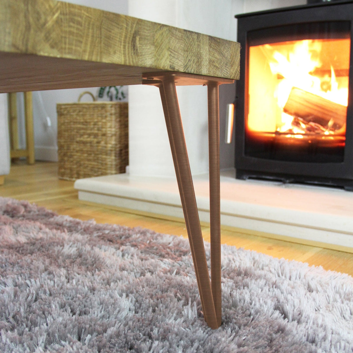 Antique copper hairpin legs with a sleek 2-prong design, supporting a wooden tabletop in a cozy, warm living room setting