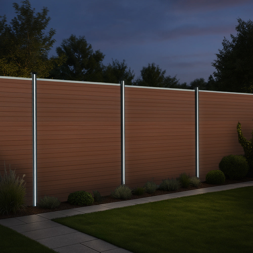 Brown composite fence panels with angled pieces and illuminated LED posts, set in a landscaped yard at dusk