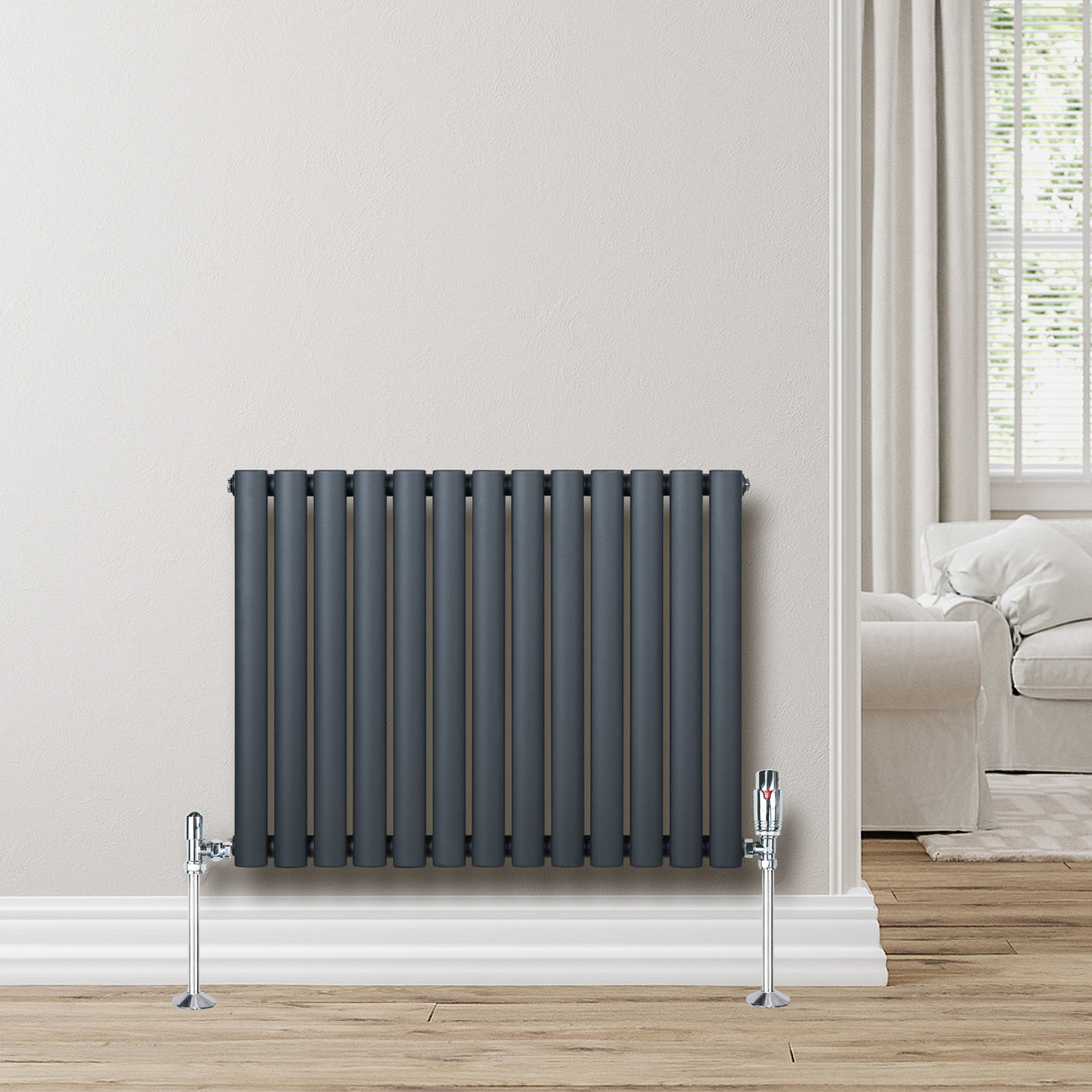 Anthracite grey oval single column radiator with sleek vertical bars and chrome valves, mounted on a light wall in a cozy room setting