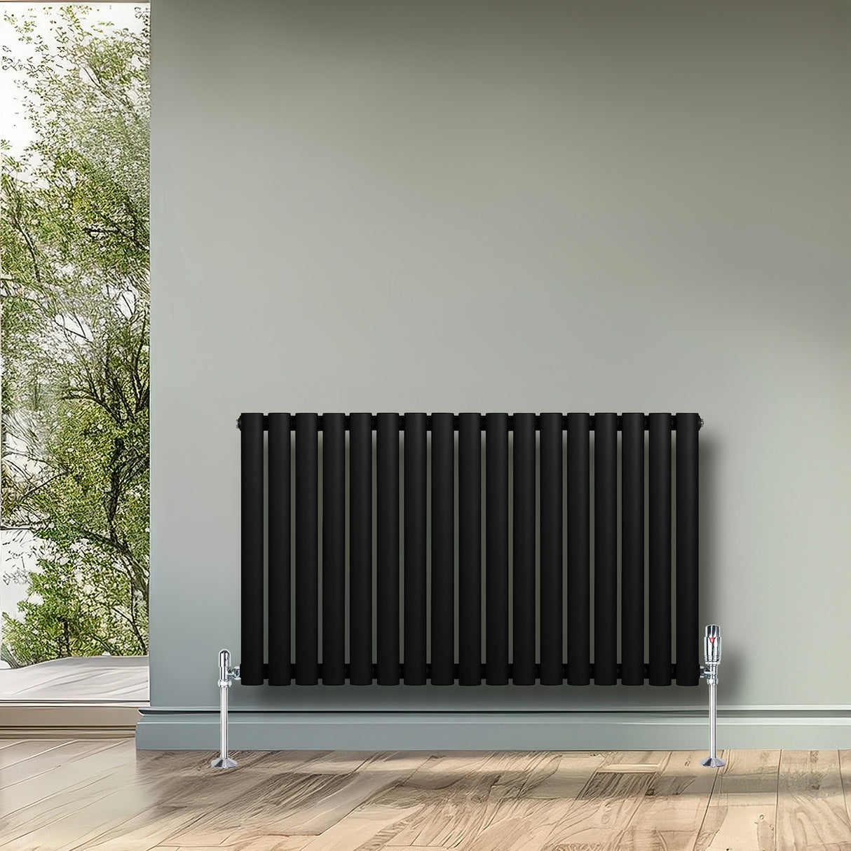 Sleek black oval single column radiator with polished valves, mounted on a light gray wall, complementing a natural setting