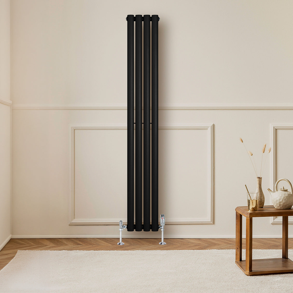 Sleek black oval single column radiator standing against a light wall, complemented by chrome valves and a wooden table nearby