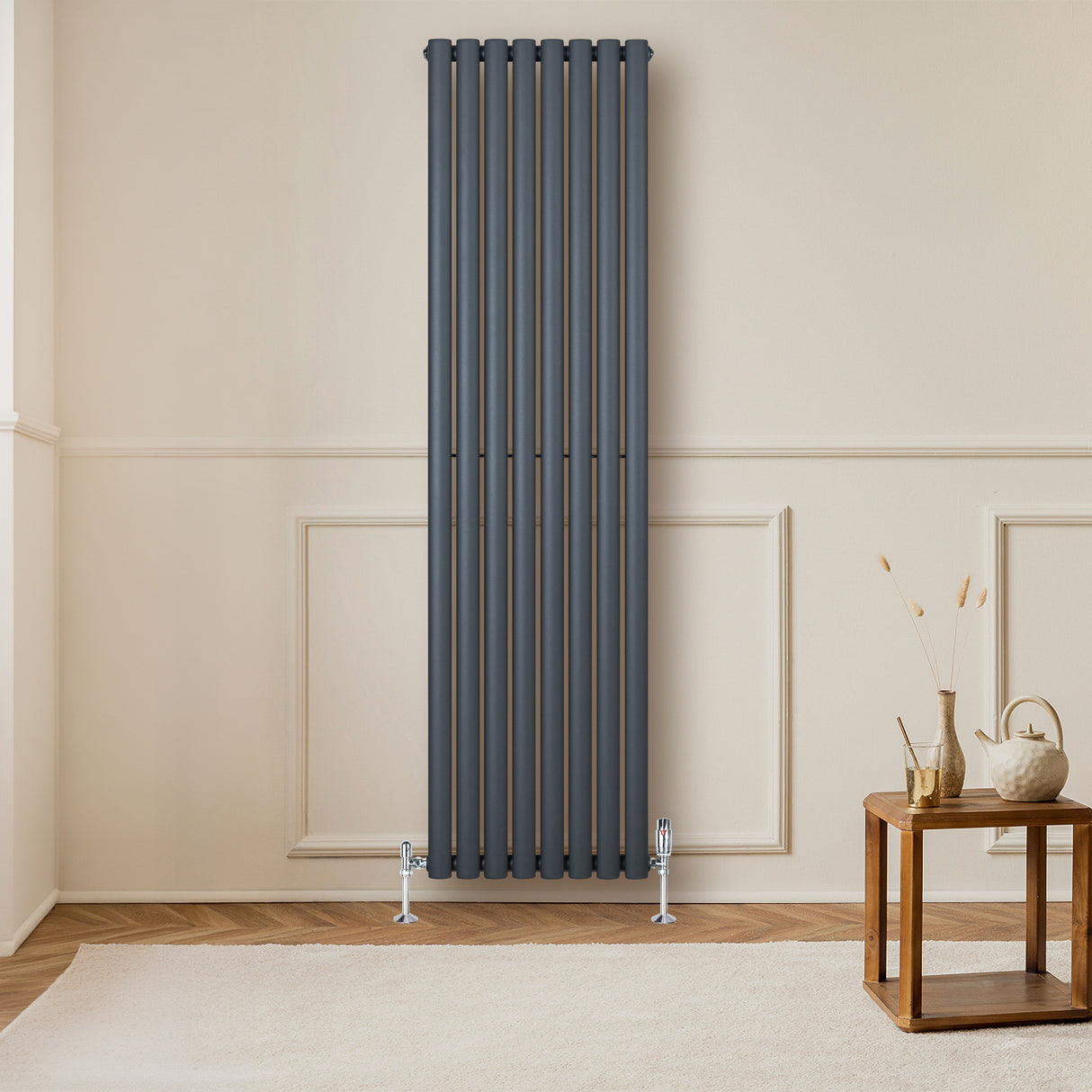 Anthracite grey oval single column radiator mounted on a wall, complemented by stylish valves and a wooden side table in a cozy room