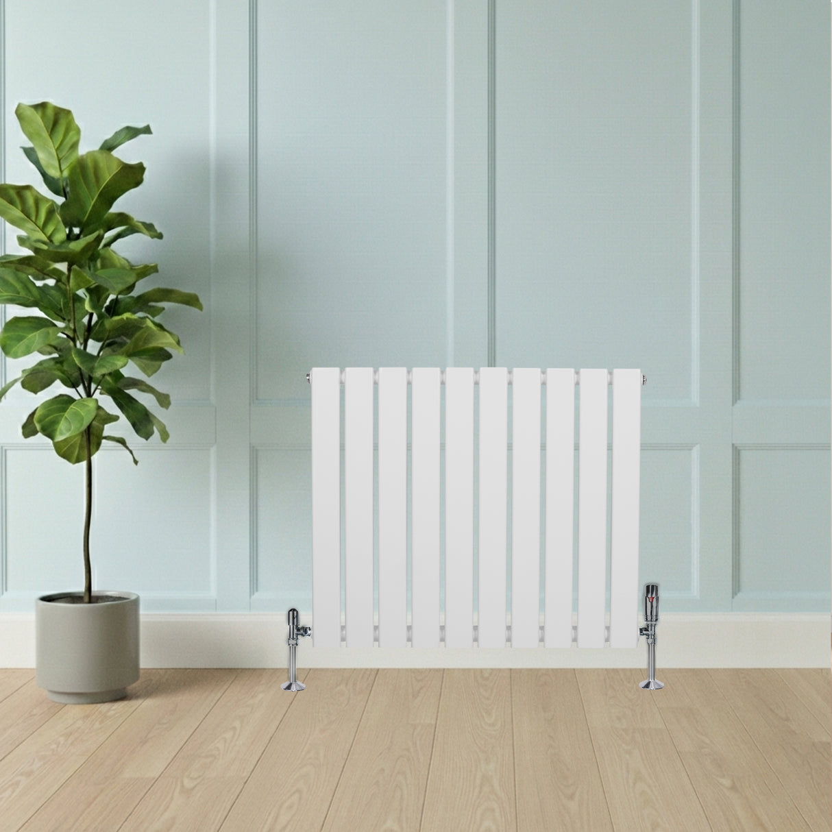 Sleek white flat single column radiator with chrome valves, set against a light blue wall and wooden floor, complemented by a green plant