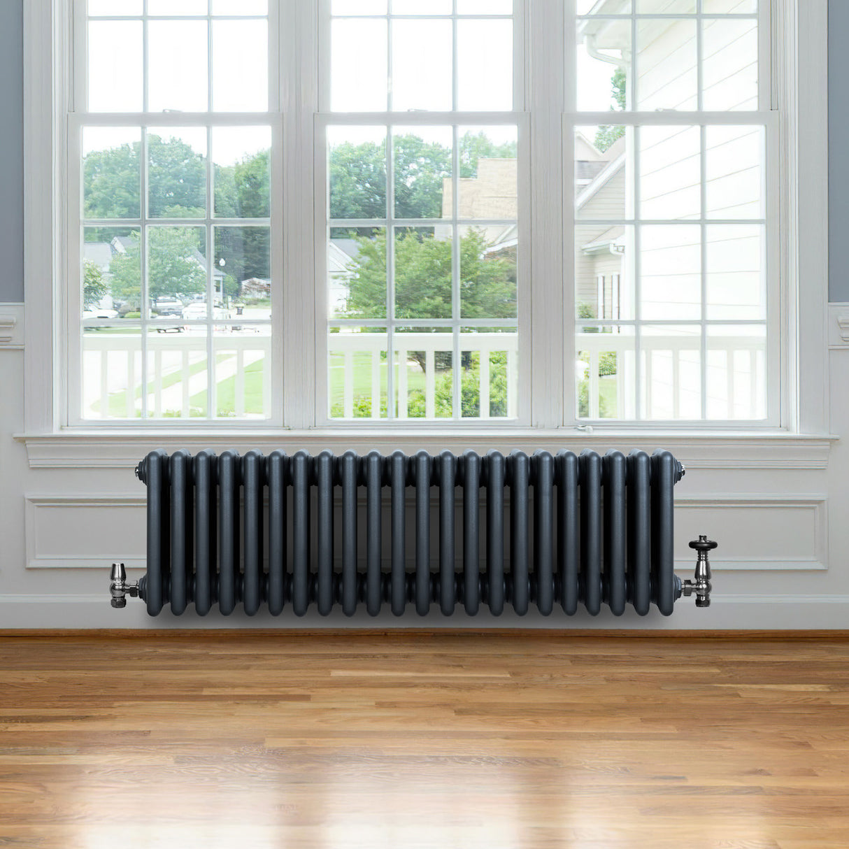 Traditional anthracite grey 4 column radiator with valves, featuring a sleek design, installed beneath a large window in a bright room