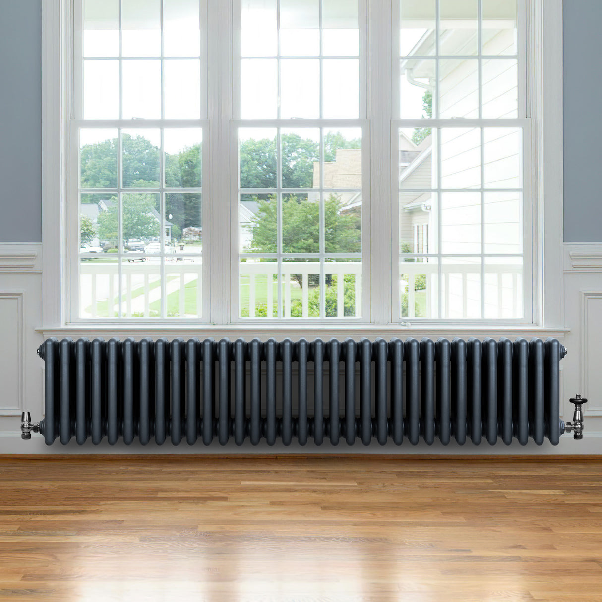 Traditional anthracite grey 4 column radiator with valves, featuring a sleek, smooth finish, positioned beneath a large window in a bright room