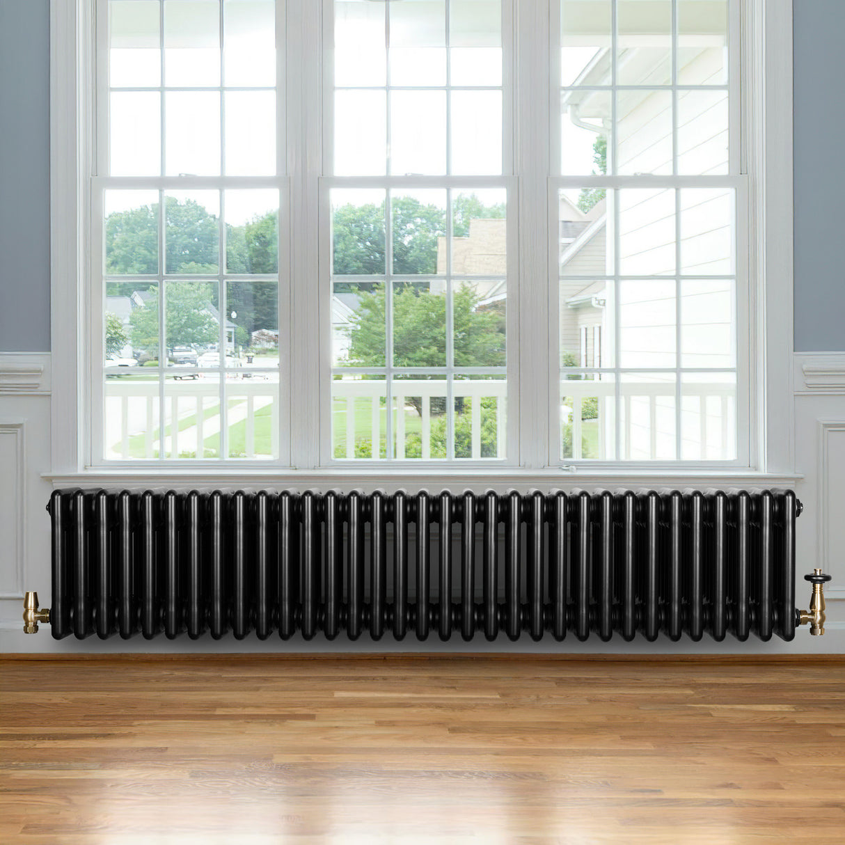 Traditional black 4 column radiator with a glossy finish, positioned beneath a large window, enhancing a cozy interior space