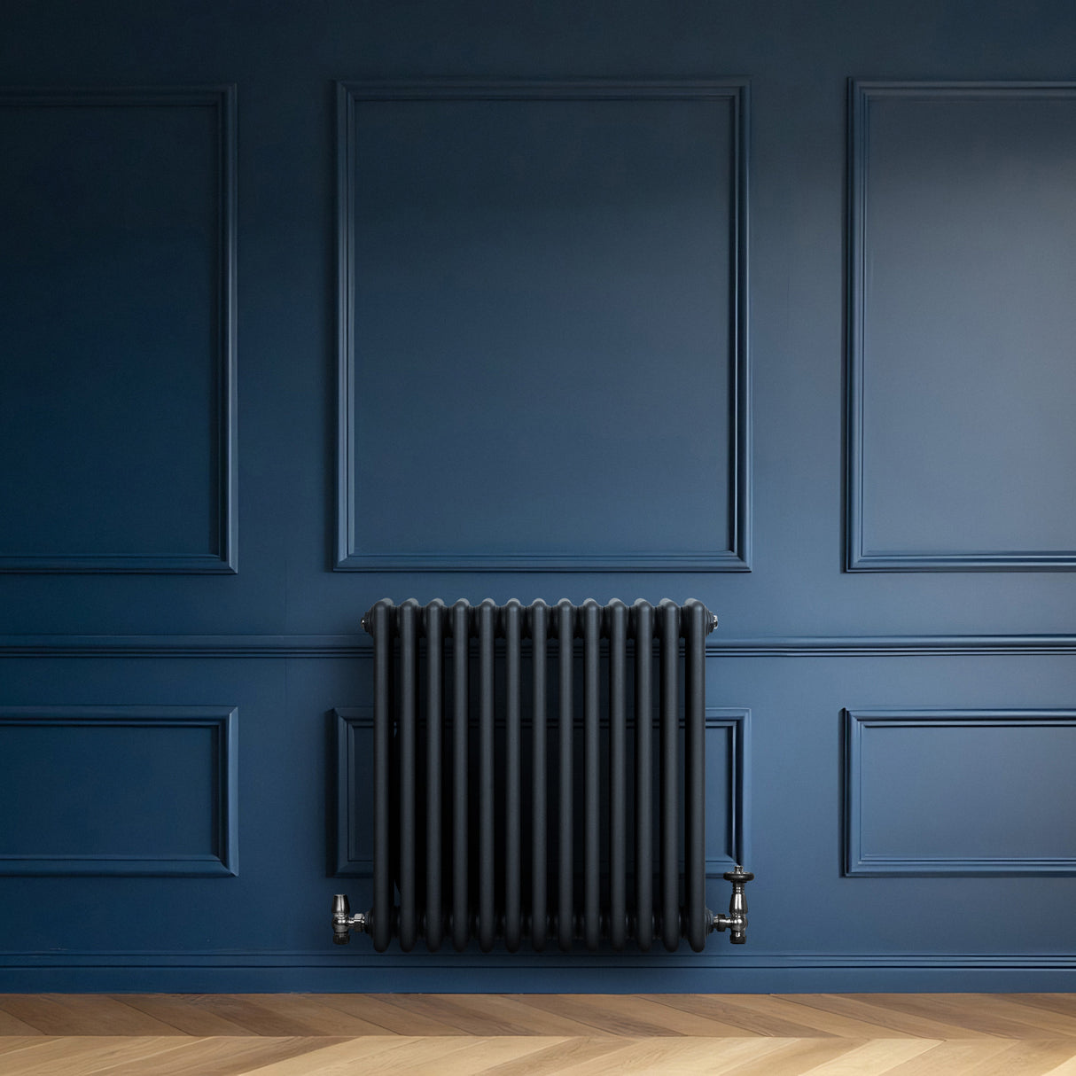 Traditional anthracite grey 4 column radiator mounted on a deep blue wall, featuring a sleek, textured finish and vintage-style valves