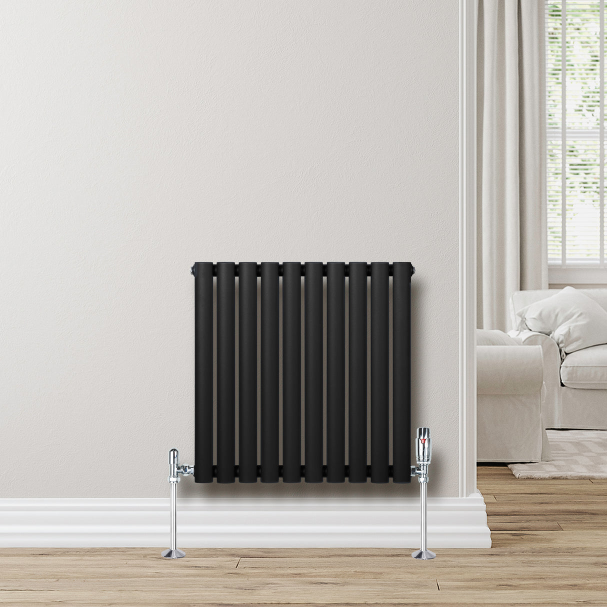 Sleek black oval single column radiator, 600 x 600mm, mounted on a light wall, complemented by chrome valves and a warm wood floor