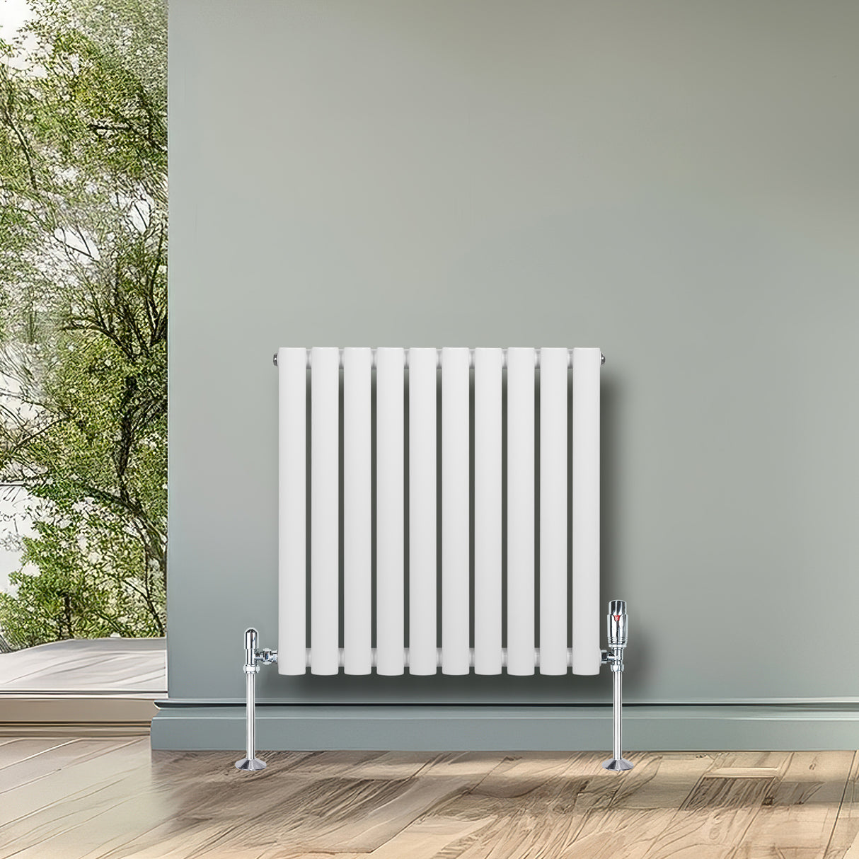 Sleek white oval single column radiator with vertical bars, mounted on a wall in a bright room with wooden flooring and greenery outside