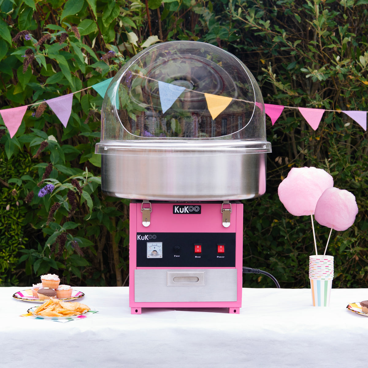 Cotton candy machine in pink with a clear dome, surrounded by colorful bunting and treats on a table outdoors