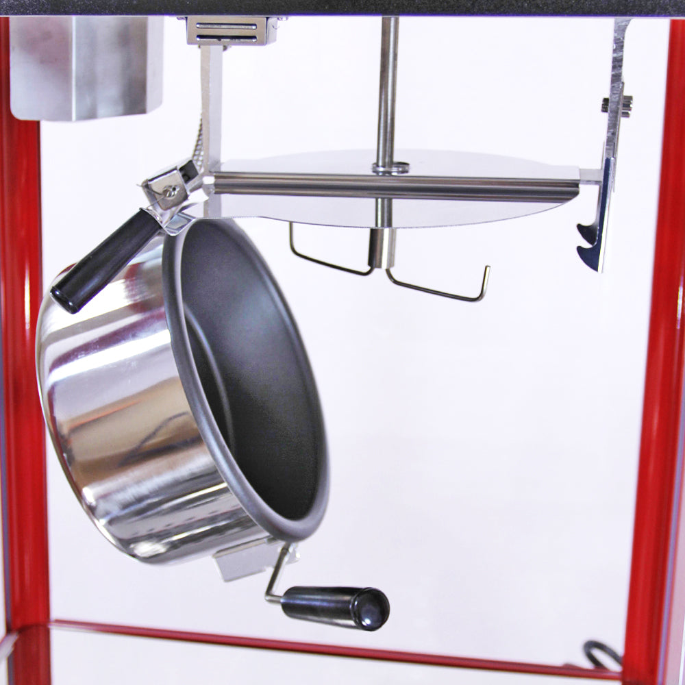 Stainless steel popcorn kettle with a black interior, suspended from a red popcorn machine frame, featuring a manual crank handle