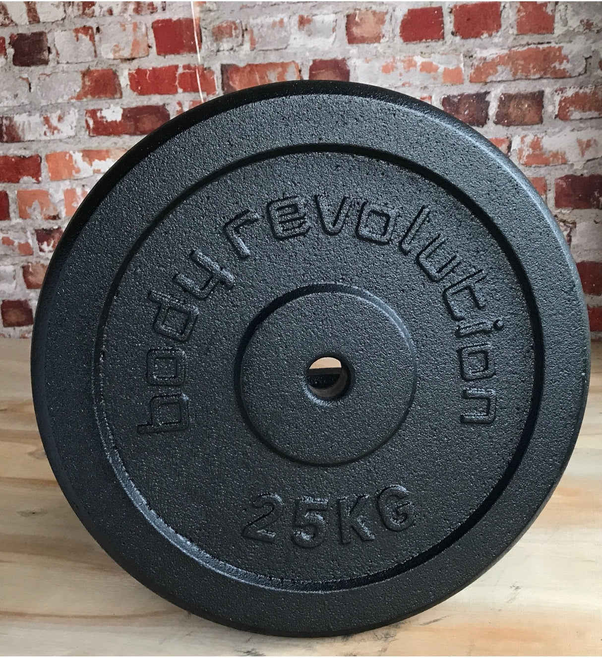 Heavy cast iron weight plate, 25kg, featuring a textured black surface and embossed "body revolution" branding, ideal for strength training