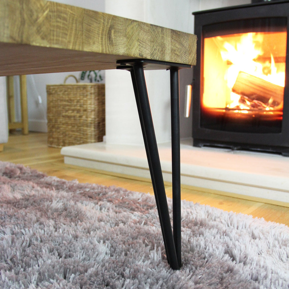Raw steel hairpin legs with a sleek, minimalist design supporting a wooden tabletop, set against a cozy fireplace backdrop