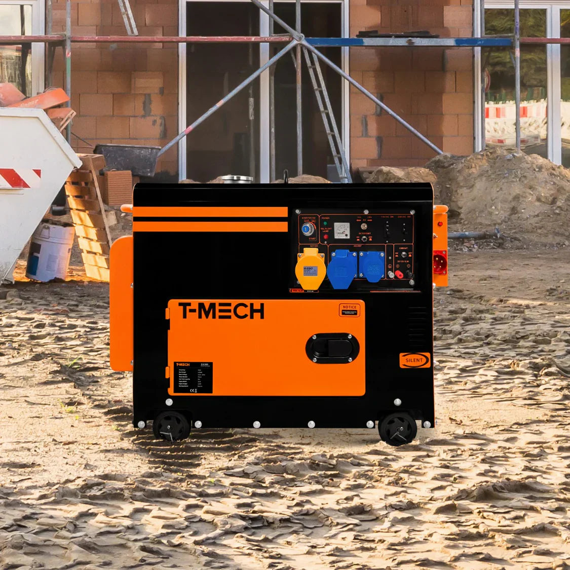 Portable T-MECH generator in black and orange, featuring control panel with gauges and outlets, set on a sandy construction site