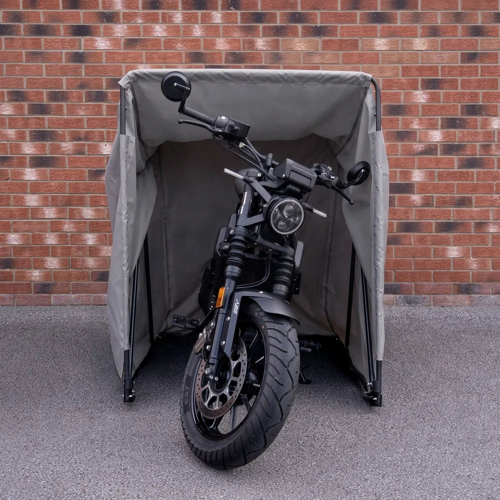 A sleek black motorbike parked inside a waterproof gray tent, featuring sturdy poles and a textured fabric, against a brick wall
