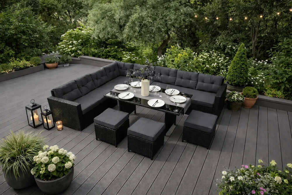 Stylish outdoor dining set with a black sectional sofa, glass table, and elegant table settings surrounded by lush greenery