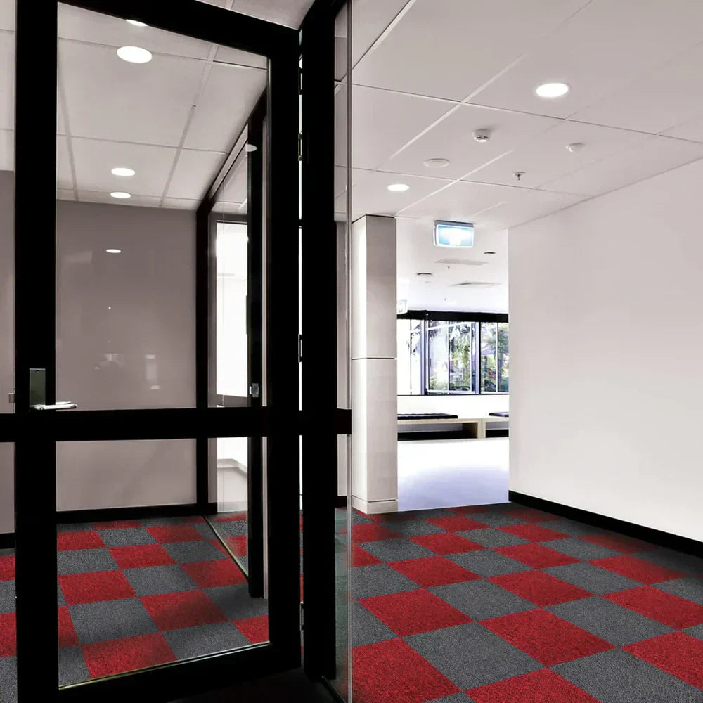 Modern office entrance featuring a checkerboard pattern of red and gray carpet tiles, sleek glass doors, and bright overhead lighting