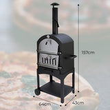 Black KuKoo outdoor pizza oven with stainless steel door, chimney, and wheels, set against a blurred pizza backdrop