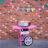 Bright pink cotton candy machine with stainless steel bowl, set against a brick wall and colorful triangular bunting