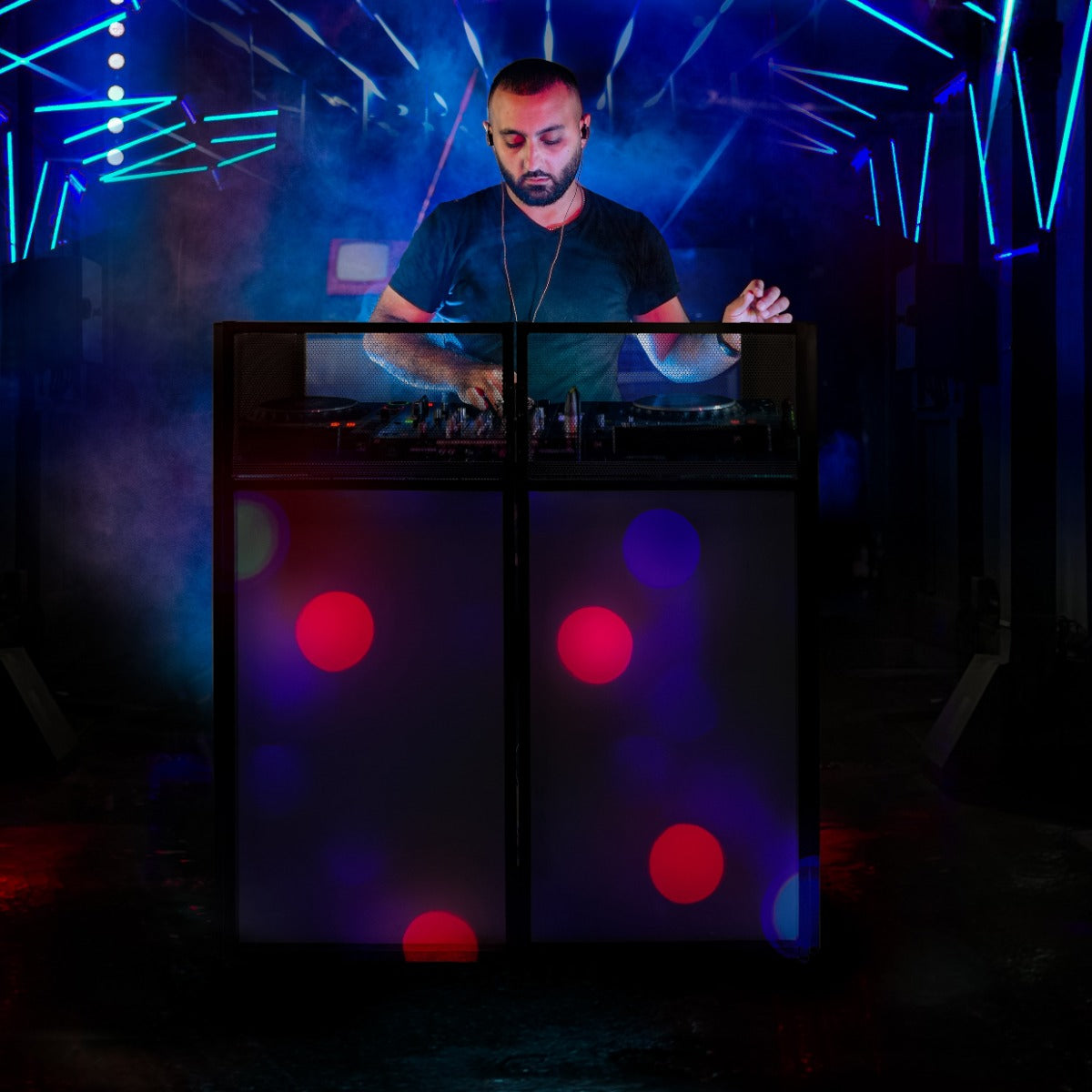 A DJ stands behind a sleek black booth with colorful lights and vibrant bokeh effects, creating an energetic party atmosphere