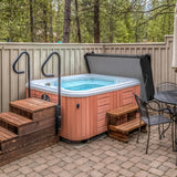 Black 2m hot tub spa cover resting on a wooden deck, surrounded by trees and a stone patio with outdoor seating