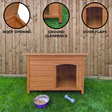 Small wooden dog kennel with a slanted roof, ground clearance, and door flaps, set on grass against a wooden fence