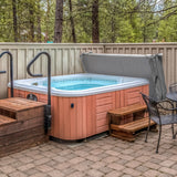 Grey hot tub spa cover resting on a 2.2m hot tub, surrounded by wooden steps and a stone patio in a serene outdoor setting