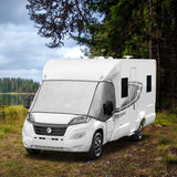 White motorhome parked in a forest clearing, featuring large windows and a sleek design, surrounded by tall green trees and a serene lake