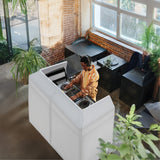 Sleek white DJ booth with a musician mixing tracks, surrounded by greenery and industrial-style decor in a bright space