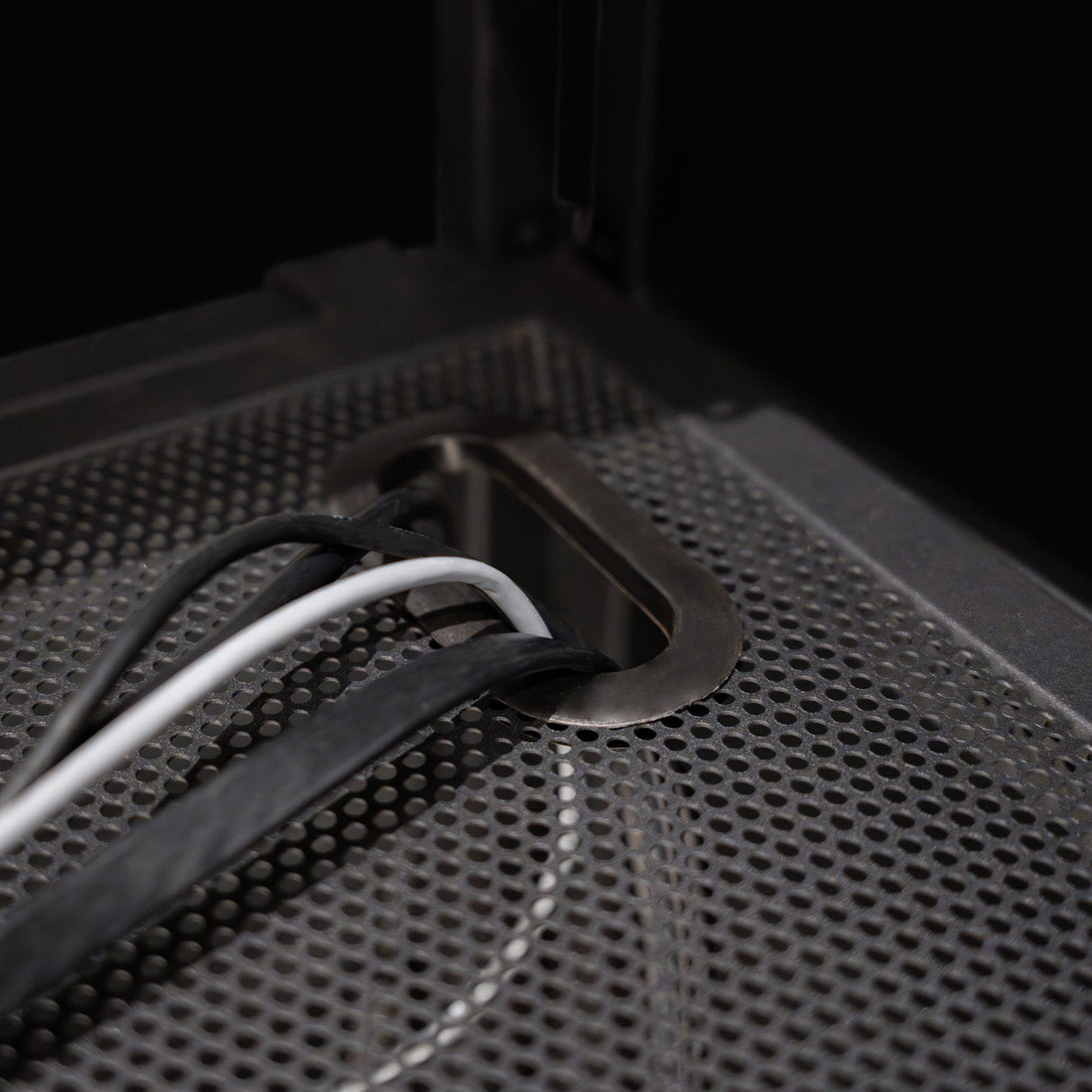 Metal cable management grommet on a textured black DJ booth surface, featuring multiple cables in white and black colors