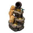 Two playful golden retriever puppies drink from a cascading electric water feature with a rustic stone finish and a bird perched nearby