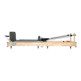 Wooden Pilates reformer with a sleek gray padded surface, featuring adjustable straps and a minimalist design for effective workouts