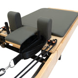 Reformer Pilates machine with a sleek wooden frame, gray padded surface, and adjustable straps for versatile workouts