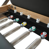 Close-up of a massage table's adjustable springs and colorful knobs, showcasing a sleek black surface and natural wood frame