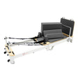 Aluminium Pilates reformer machine with gray padding, adjustable foot bar, and resistance straps, designed for versatile workouts