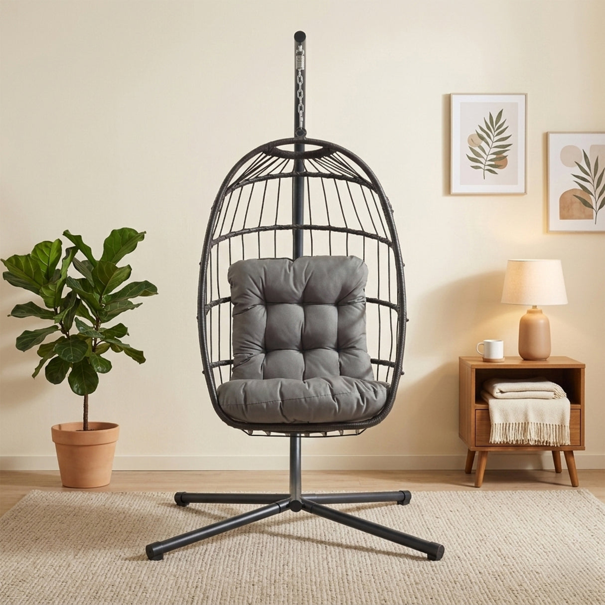 Stylish black rattan hanging egg chair with a plush gray cushion, set against a light wall and surrounded by indoor plants and decor