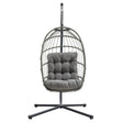Stylish grey rattan hanging egg chair with plush cushion, featuring a sturdy metal stand and a modern, airy design for relaxation