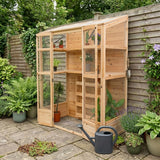 Victorian greenhouse made of natural wood with glass panels, surrounded by lush greenery and potted plants, featuring a watering can nearby