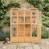 Victorian greenhouse made of natural wood with glass panels, showcasing plants inside, surrounded by lush greenery and stone pathway