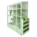 Victorian-style greenhouse in soft green wood, featuring multiple shelves, glass panels, and potted plants for gardening enthusiasts