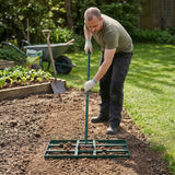 Man using a green 100cm lawn leveller on a garden bed, leveling soil with a sturdy metal frame and long handle, surrounded by greenery